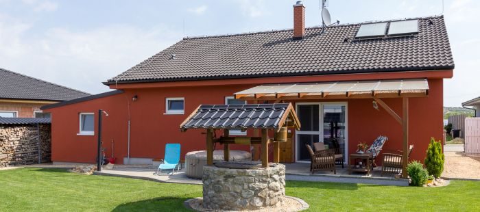 Bungalov s červenou fasádou a studnou na zahradě